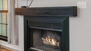 Ein modernes Wohnzimmer mit Kamin, Wandfernseher und einem fenster mit Vorhängen.
