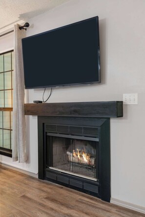 Un caminetto con una televisione montata sopra, una finestra con tende e un pavimento in legno.