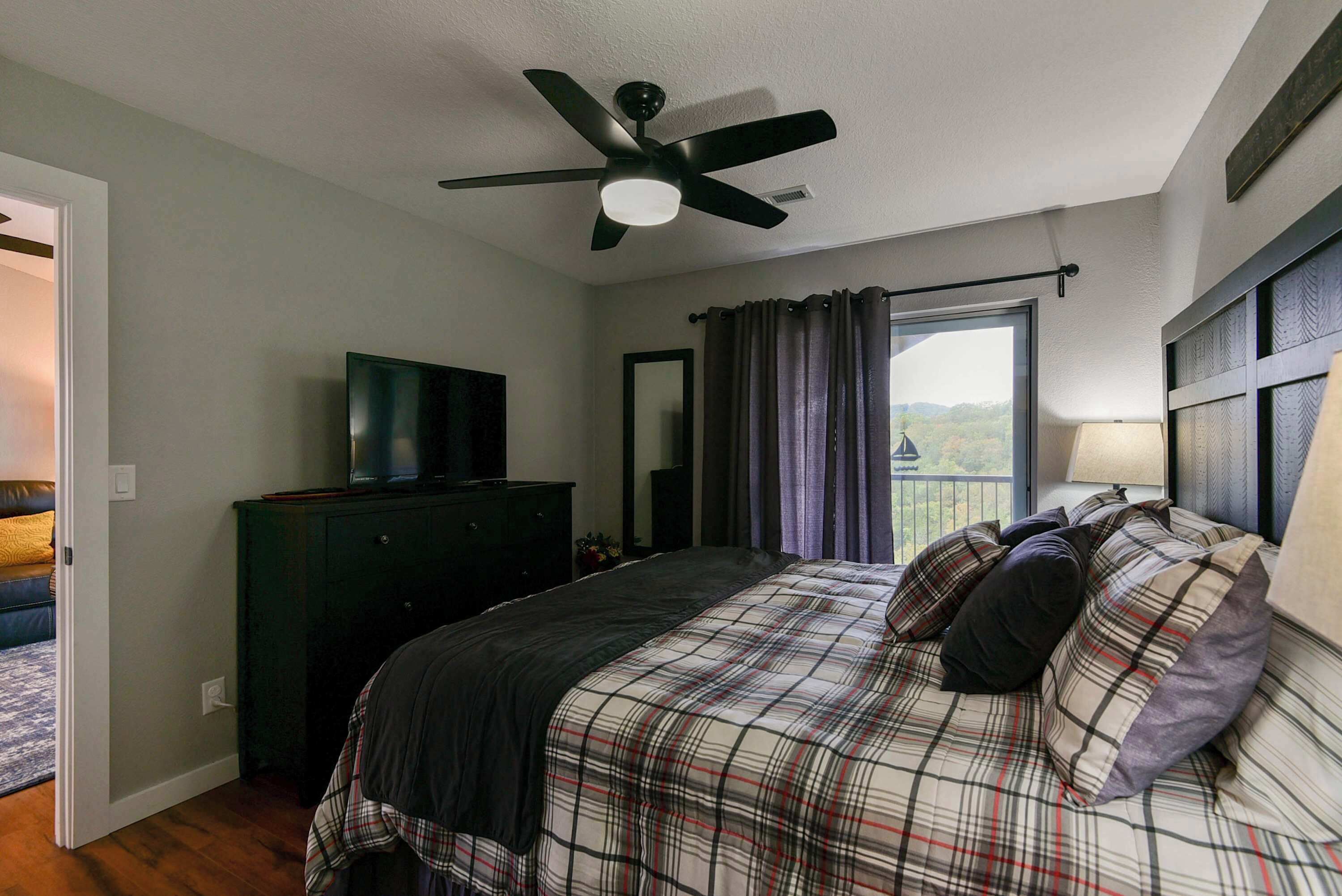 A bedroom with a bed, a ceiling fan, a dresser, a TV, and a window with curtains.