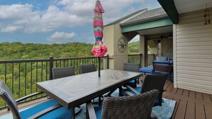 Een terras met een tafel en stoelen, een kleurrijke parasol, en uitzicht op een bebost gebied.
