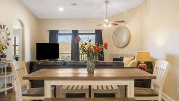 Un coin repas avec une table et des chaises en bois, un canapé, un téléviseur et un vase rempli de fleurs.