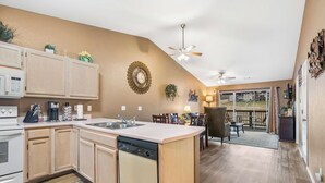 A kitchen with wooden cabinets, a dishwasher, and a central island. There is a dining area with chairs and a table, and a view of a balcony with a railing. - Stunning Water View – Pet Friendly, Indoor Pool (Branson)