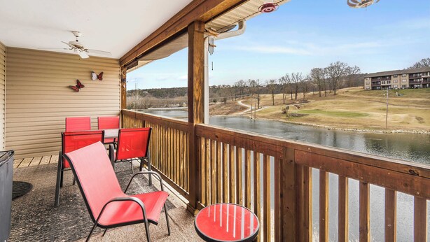 A covered outdoor area with wooden railings, red chairs, and a small table. - Stunning Water View – Pet Friendly, Indoor Pool (Branson)
