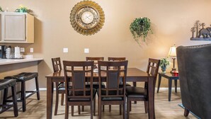 A dining area with a wooden table and chairs, a decorative wall clock, and a small plant. - Stunning Water View – Pet Friendly, Indoor Pool (Branson)