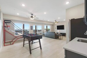 Un vaste espace de vie comprenant une table de baby-foot, un balcon avec vue et une cuisine moderne.