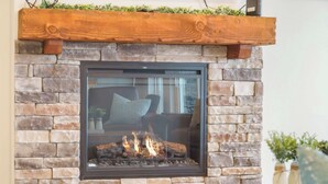A stone fireplace with a glass front, a wooden mantel, and a table in front. - Hilltop Haven at Table Rock – Lake Views & Nearby Branson’s Best Attractions (Branson)