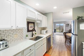 Una cocina con armarios blancos, un tostador, un fregadero y un refrigerador.