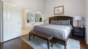 Een slaapkamer met een groot bed, een bankje, een nachtkastje, een lamp en een schilderij aan de muur.