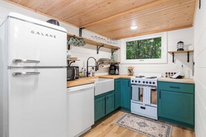 A kitchen with a Galanz refrigerator, a stove, a sink, and teal cabinets.
