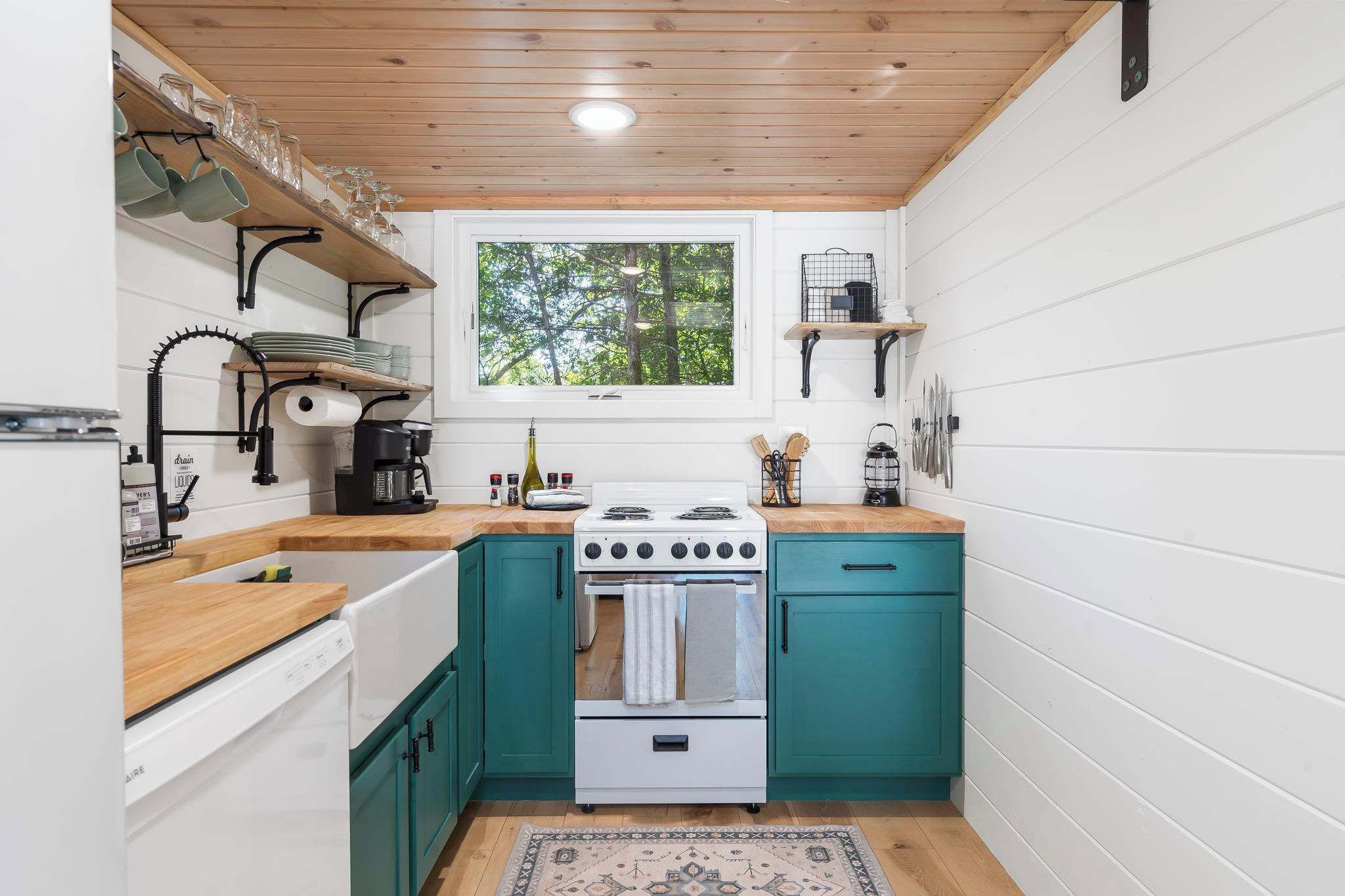 A compact kitchen with teal cabinets, a white stove, and a window overlooking greenery.