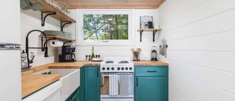 A compact kitchen with teal cabinets, a white stove, and a window overlooking greenery.