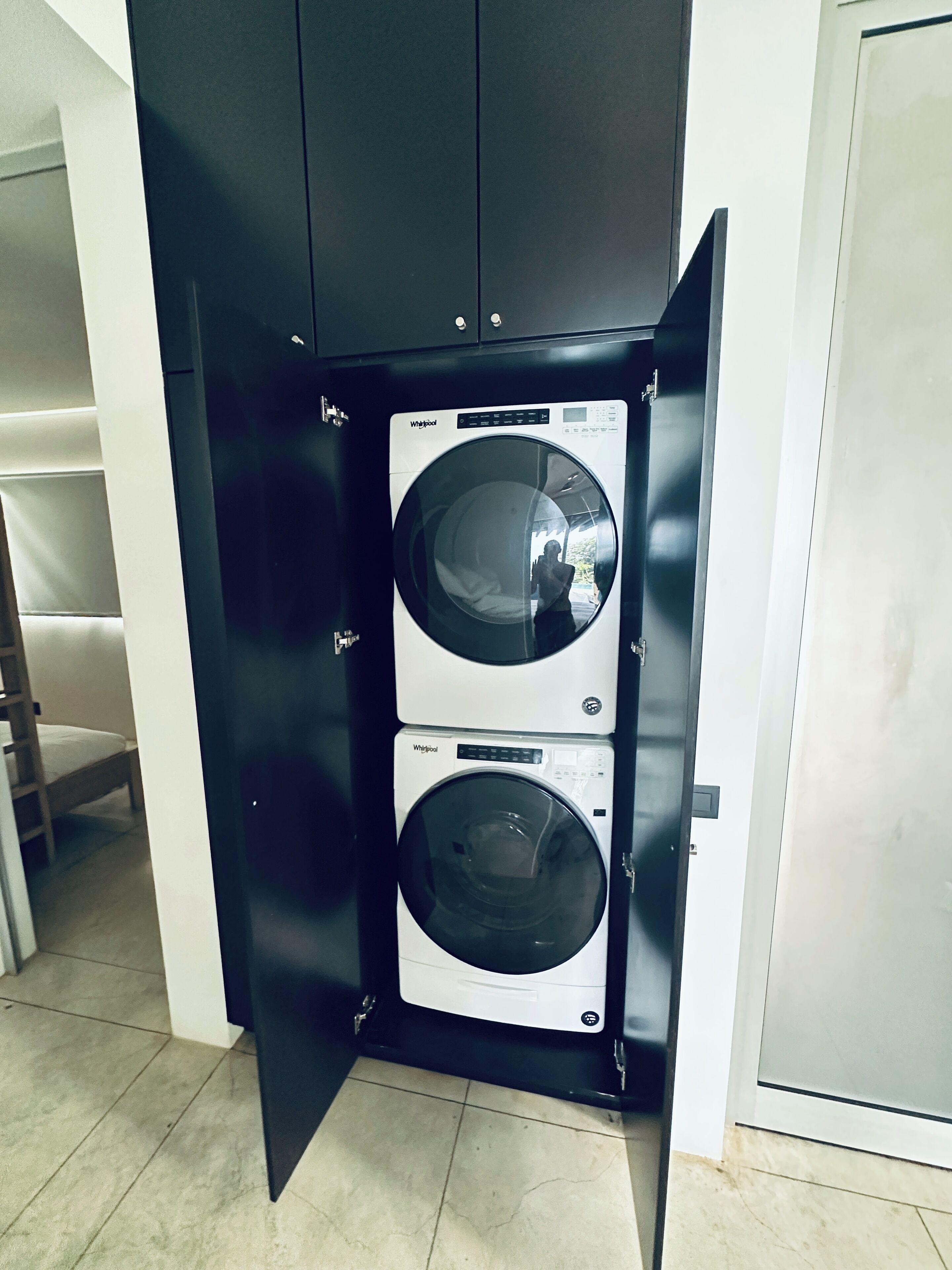 Un lavadero pequeño con dos lavadoras y secadoras Whirlpool apiladas, una escalera de madera y una puerta blanca.