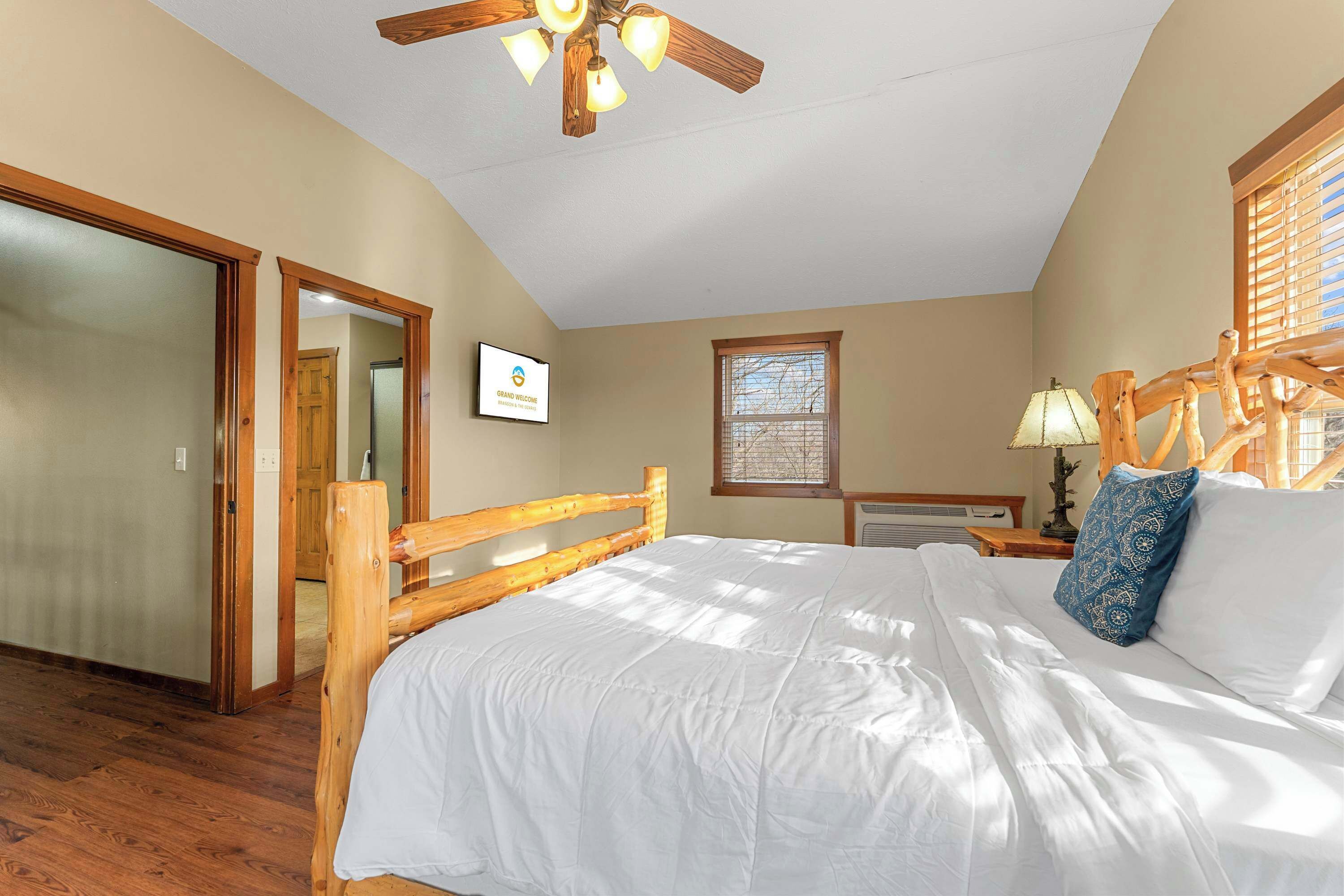 A bedroom with a wooden bed, a ceiling fan, a window with blinds, and a door leading to another room.
