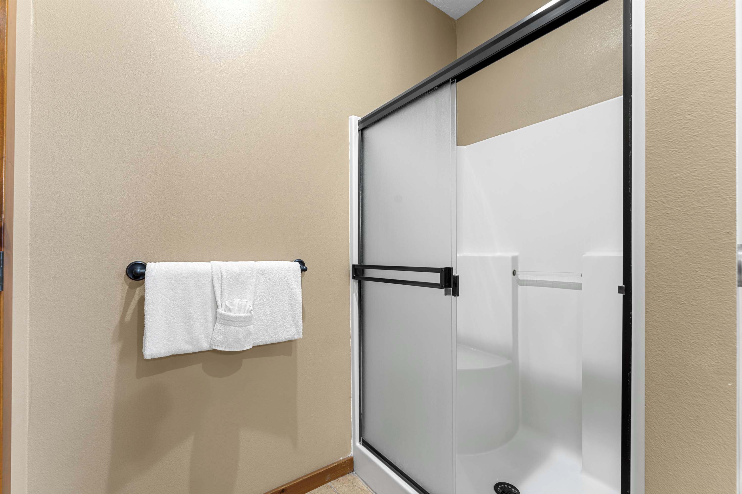 A bathroom with a glass shower enclosure, a towel rack with a white towel, and beige walls.