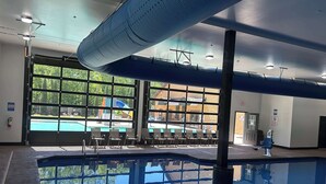An indoor swimming pool with clear glass walls, a view of an outdoor pool, and a ceiling with a unique design. - Royal Moose Lodge – A Grand Adventure for 20! (Branson)