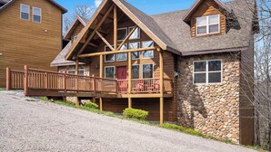A log cabin with a stone exterior, a wooden deck, and a red door. - Royal Moose Lodge – A Grand Adventure for 20! (Branson)