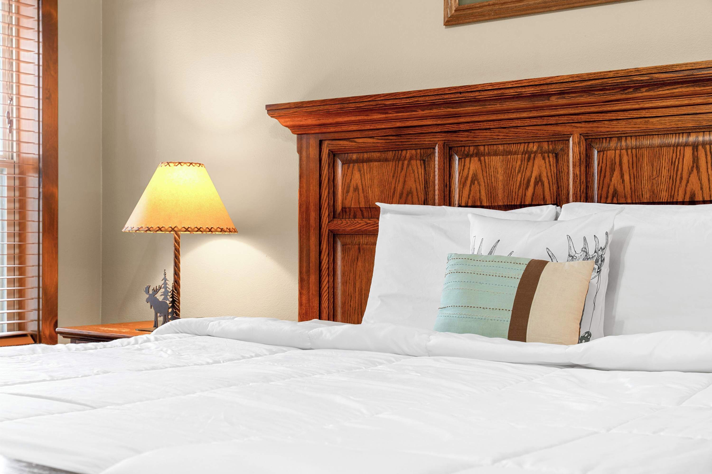A neatly made bed with white bedding, a wooden headboard, and a bedside lamp.