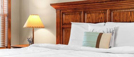 A neatly made bed with white bedding, a wooden headboard, and a bedside lamp.
