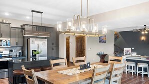 A modern kitchen with grey cabinets, a wooden dining table, and a chandelier.