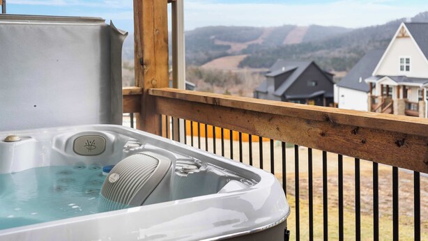 A hot tub on a wooden deck with a view of houses and hills in the background.