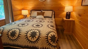 A cozy wooden room with a bed, two nightstands, and a wall-mounted lamp. - Cave Run Lodge - Near Lake - Playground & Fire Pit- Cabin #5 (Morehead)