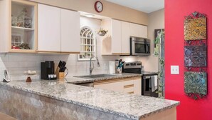 Una cocina con encimera de granito, armarios blancos, microondas y una pared de acento roja.