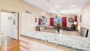 Una cocina amplia con encimera de granito, un comedor con mesa y sillas, y una sala de estar con sofá y televisor.