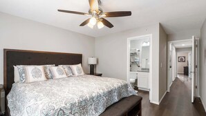 A bedroom with a large bed, a ceiling fan, and a hallway leading to a bathroom. - Urban Farmhouse | Refreshing Pool! (Branson)