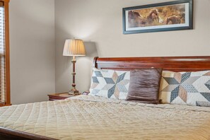 Un dormitorio con cabecera de madera, colcha acolchada, lámpara de noche y un cuadro enmarcado en la pared.