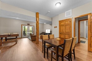 A spacious living room with a wooden dining table, comfortable seating, and a television.