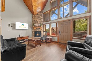 Una sala de estar amplia con chimenea de piedra, techo de madera y ventanas grandes.