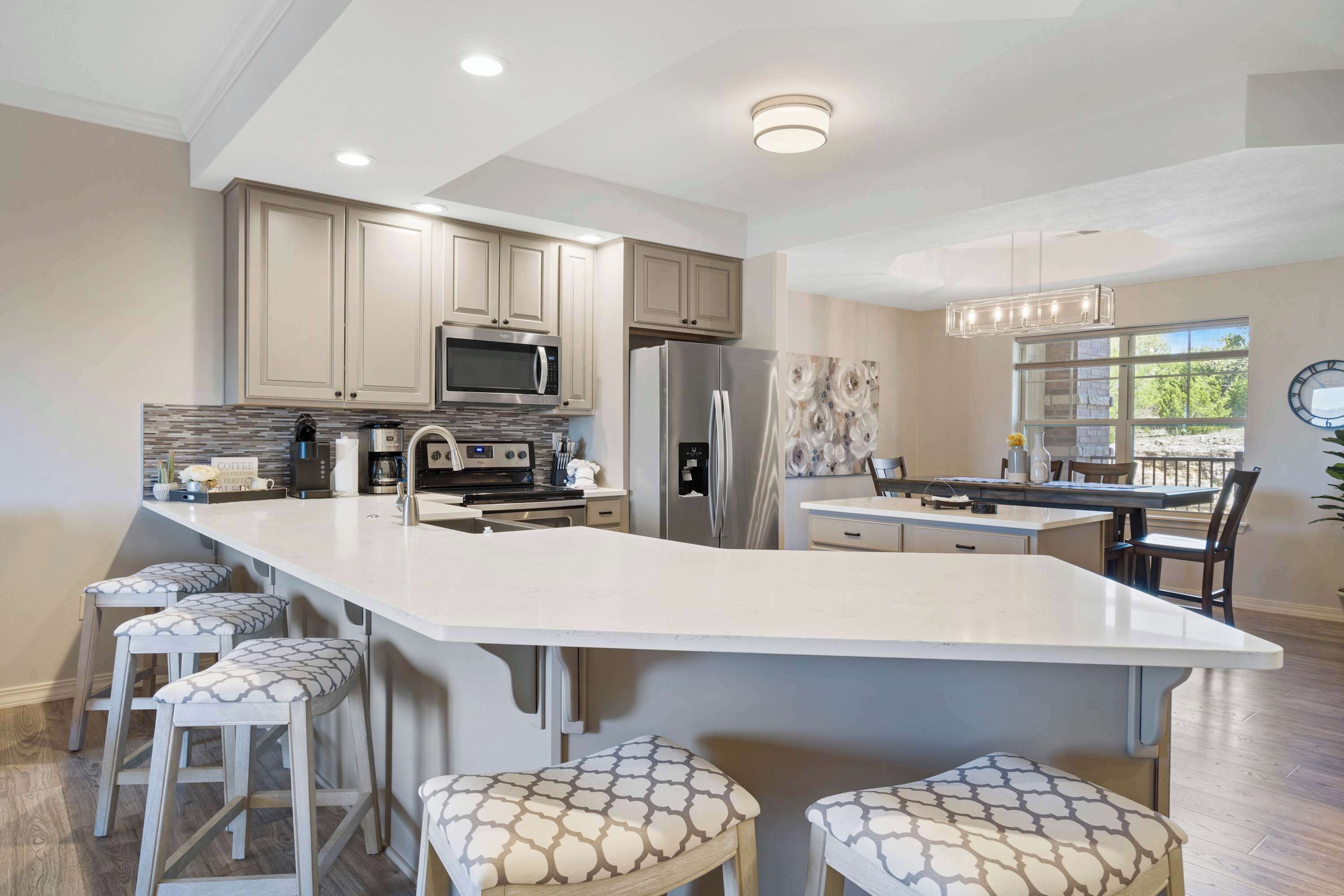 A modern kitchen with a large island, bar stools, stainless steel appliances, and a view to the outside.