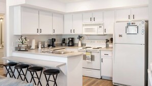 A modern kitchen with white cabinets, a central island with stools, a microwave, stove, and refrigerator. - Boatin & Floatin on Table Rock Lake in the Ozarks! (Kimberling City)