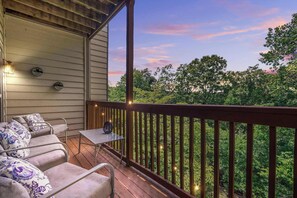 A covered outdoor seating area with a wooden deck, a table, and chairs with patterned cushions.