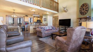 A spacious living area with a high ceiling, a fireplace, a mounted clock, and a television. - Fox Hollow Family Lodge (Branson West)