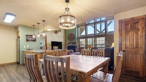 A dining area with a wooden table and chairs, a chandelier, and a stone fireplace. - Fox Hollow Family Lodge (Branson West)