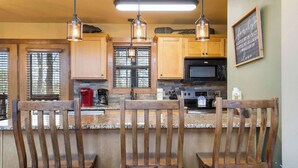 A kitchen with wooden cabinets, a granite countertop, and three wooden chairs. - Fox Hollow Family Lodge (Branson West)