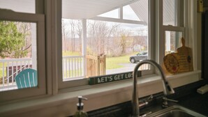 Une cuisine avec une fenêtre donnant sur un jardin, une terrasse en bois et un panneau sur lequel on peut lire : « PERDONS-NOUS ».
