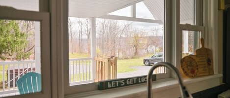 A kitchen with a window overlooking a backyard, a wooden deck, and a sign that reads "LET'S GET LOST".
