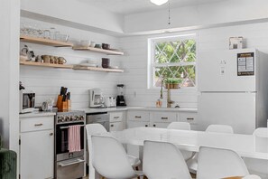 Une cuisine moderne avec des meubles blancs, une table à manger avec des chaises et une fenêtre donnant sur les arbres.