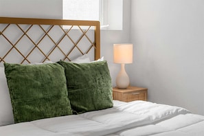 Uma cama com cabeceira de madeira, duas almofadas verdes, um edredom branco, uma luminária de cabeceira e um criado-mudo de madeira.