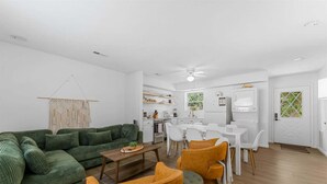 A modern living room with a green sofa, a wooden coffee table, and a dining area with white chairs and a table. - Pools/ Hot Tub / Whispering Woods Retreat (Branson)