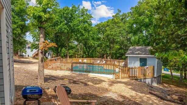 A backyard with a wooden fence, a small shed, a pool, and outdoor furniture. - Pools/ Hot Tub / Whispering Woods Retreat (Branson)