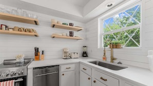 A kitchen with white cabinetry, a stainless steel range, a dishwasher, and a window with a view of greenery. - Pools/ Hot Tub / Whispering Woods Retreat (Branson)