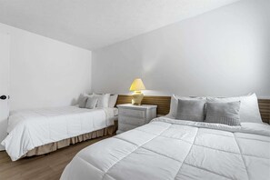 Une chambre d’hôtel avec deux lits, une table de chevet avec une lampe et une tête de lit en bois.