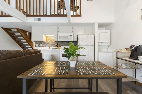 Experience a spacious living area with a wooden staircase, kitchen, dining table, and comfortable seating.