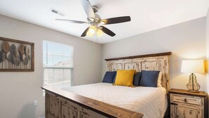Ein Schlafzimmer mit einem Bett, Deckenventilator, Nachttisch, Lampe und einem Fenster mit Jalousien.
