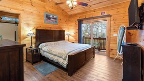 A wooden cabin room with a bed, two bedside lamps, a ceiling fan, a TV, and an exit sign. - Teal’s Treasure – Secluded Lakeside Cabin for 8! (Kirbyville)