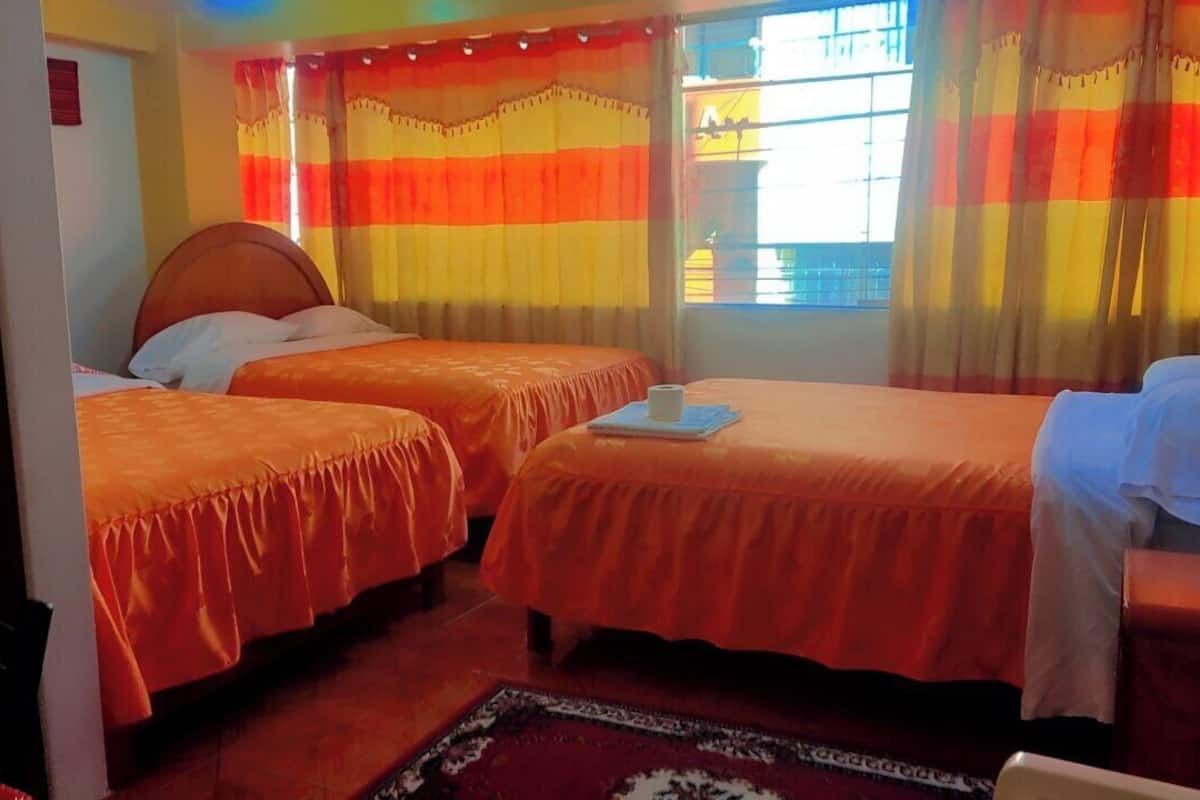 A hotel room with two beds, a window with curtains, and a small table with a cup.