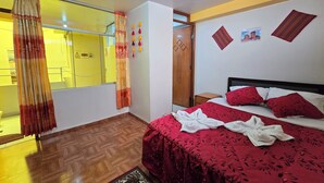 Une chambre d’hôtel avec un lit, un plancher en bois, un miroir, une armoire et une fenêtre avec des rideaux.